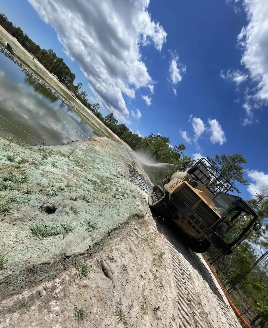 Hydroseeding applied to the slope ahead of matting installation to promote seed-to-soil contact and ensure effective erosion control.