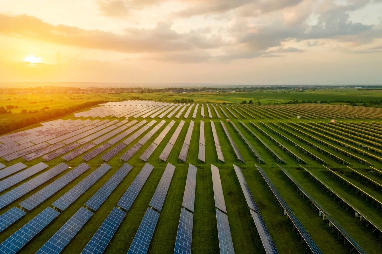 Aerial view of a utility-scale solar farm at sunset with rows of panels over grass