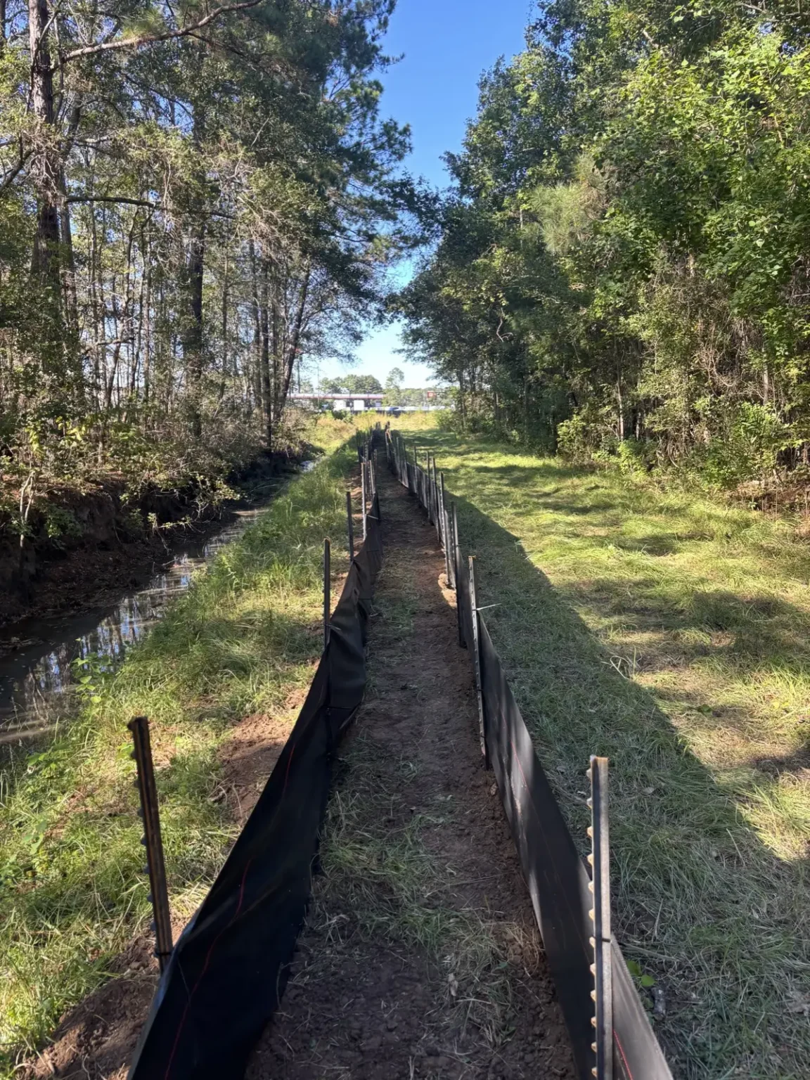Silt fence installed by Eco Express along both sides of a drainage ditch, with the fabric trenched in and backfilled at the toe